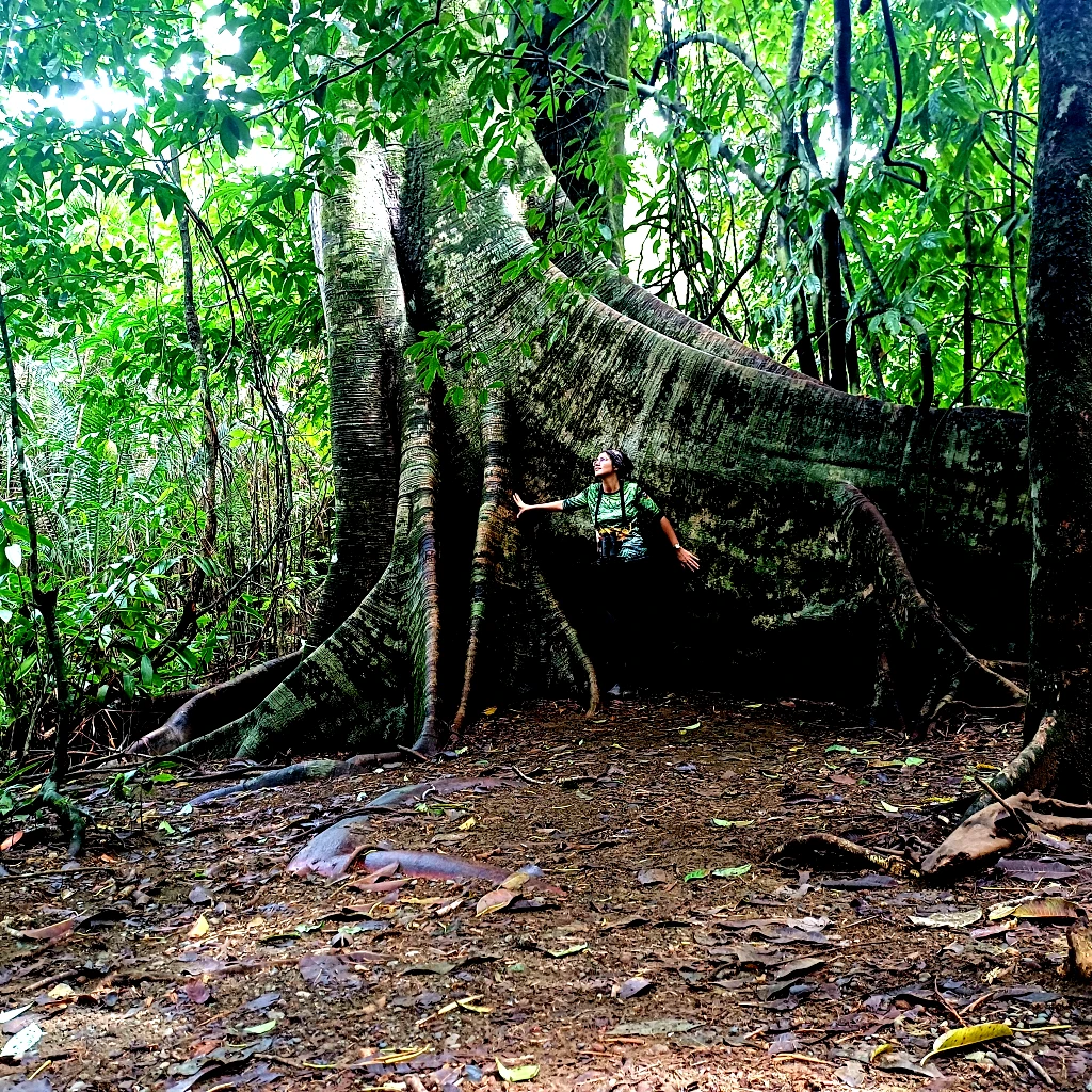 Karen Rodríguez, guide and founder of Osa Outdoors Adventures, standing beside a giant rainforest tree in Corcovado National Park, Costa Rica.